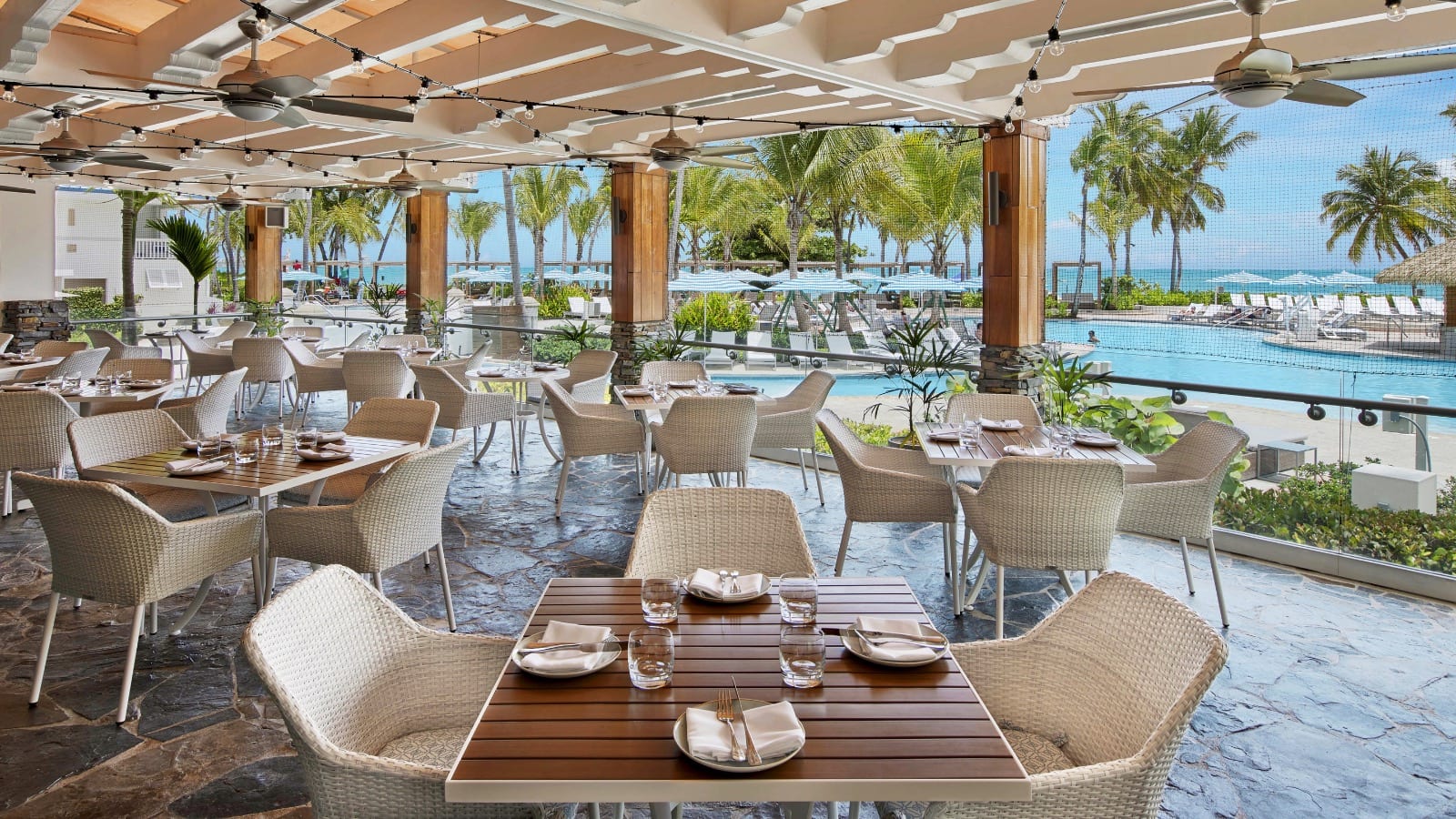 Restaurante de resort frente al mar con vista a la piscina y palmeras.